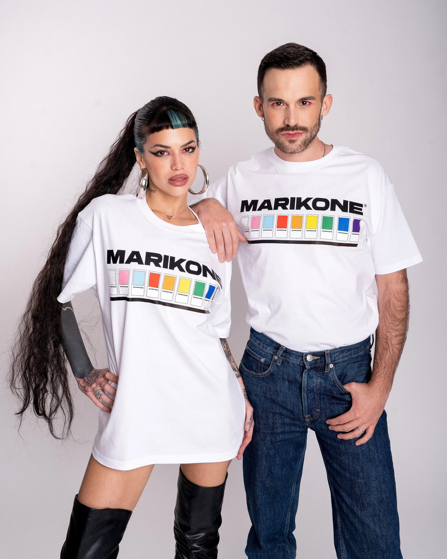 Foto de Moda Queer de un chico con sombra rosa en los ojos y una chica con larga coleta, posan juntos usando las camisetas blanca que dicen MARIKONE. Con cuadros de colores de la bandera del Orgullo LGTBIQ+ y Trans como catálogo pantone